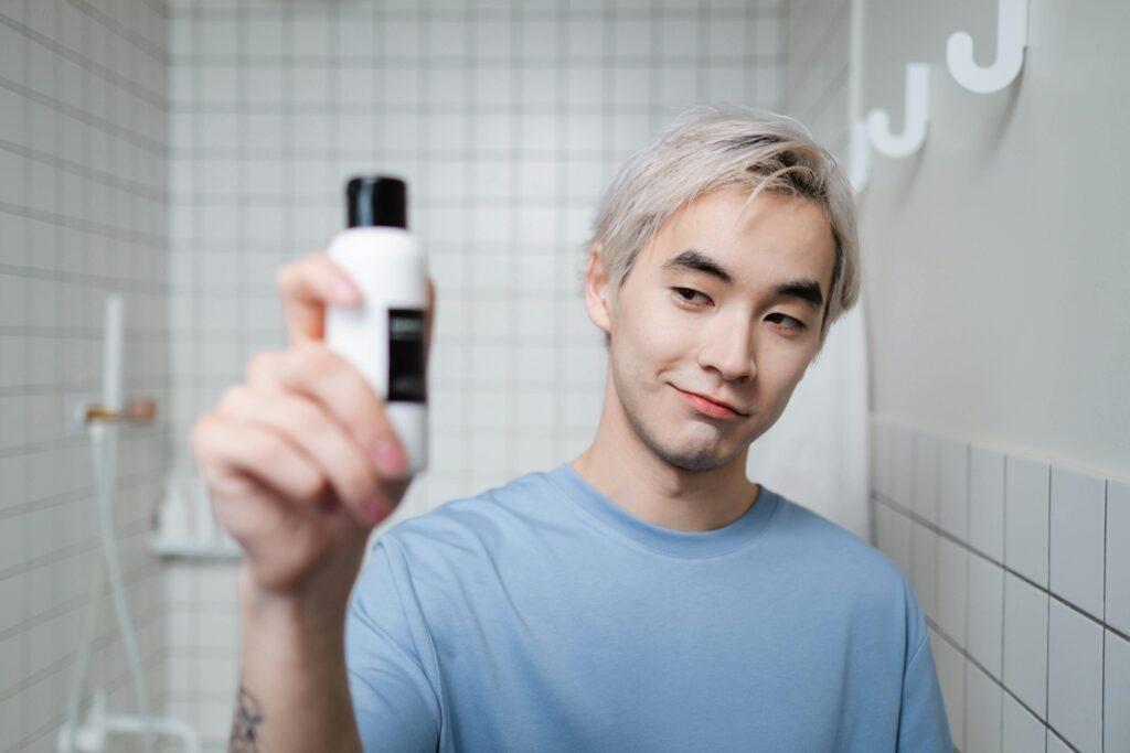 Junger Mann präsentiert ein Fläschchen mit wissenschaftlich formuliertem Hautpflegeprodukt in einem hellen, modernen Badezimmer.