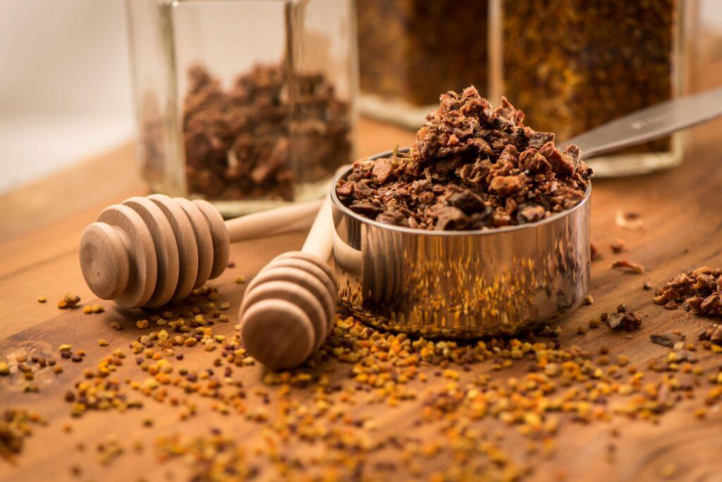 Propolis: Natürliche Rohstoffe auf Holzuntergrund mit Honiglöffel und Glasgefäßen