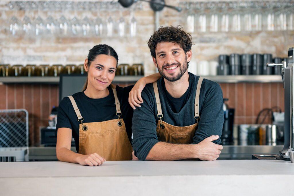 Zwei Mitarbeitende in bestickter Arbeitskleidung hinter dem Tresen
