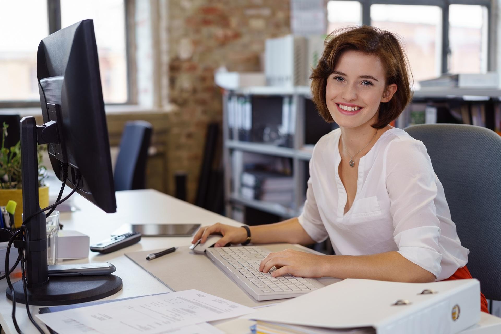 Lächelnde Mitarbeiterin arbeitet konzentriert am Schreibtisch | Klick Vinyl Eiche